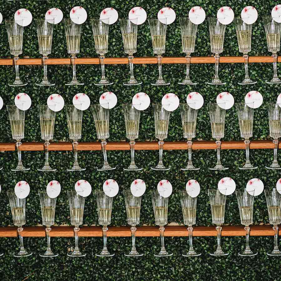 Champagne glass escort card display with round red and white cards on a greenery wall
