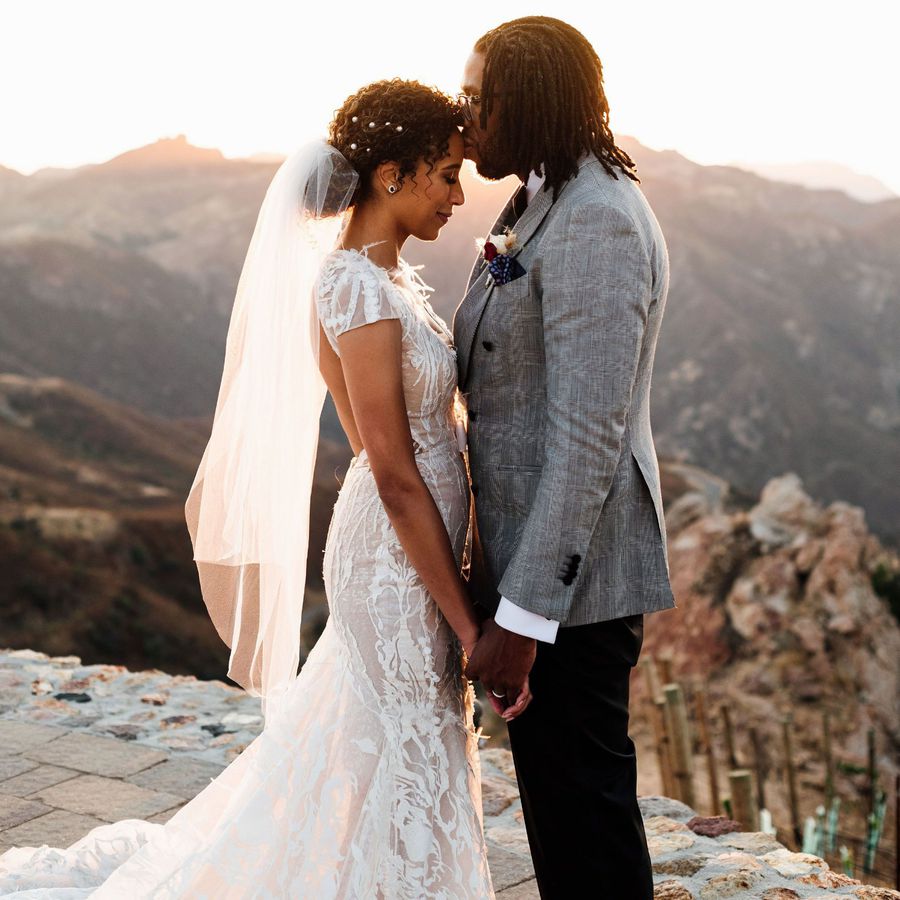 Bride and groom holding hands with groom kissing her forehead, mountains in the background