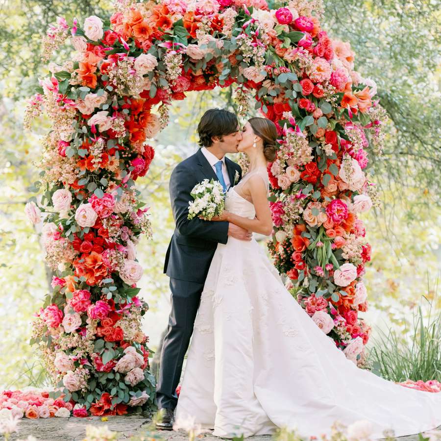 Julianna and Lee kissing in front of their pink floral arch