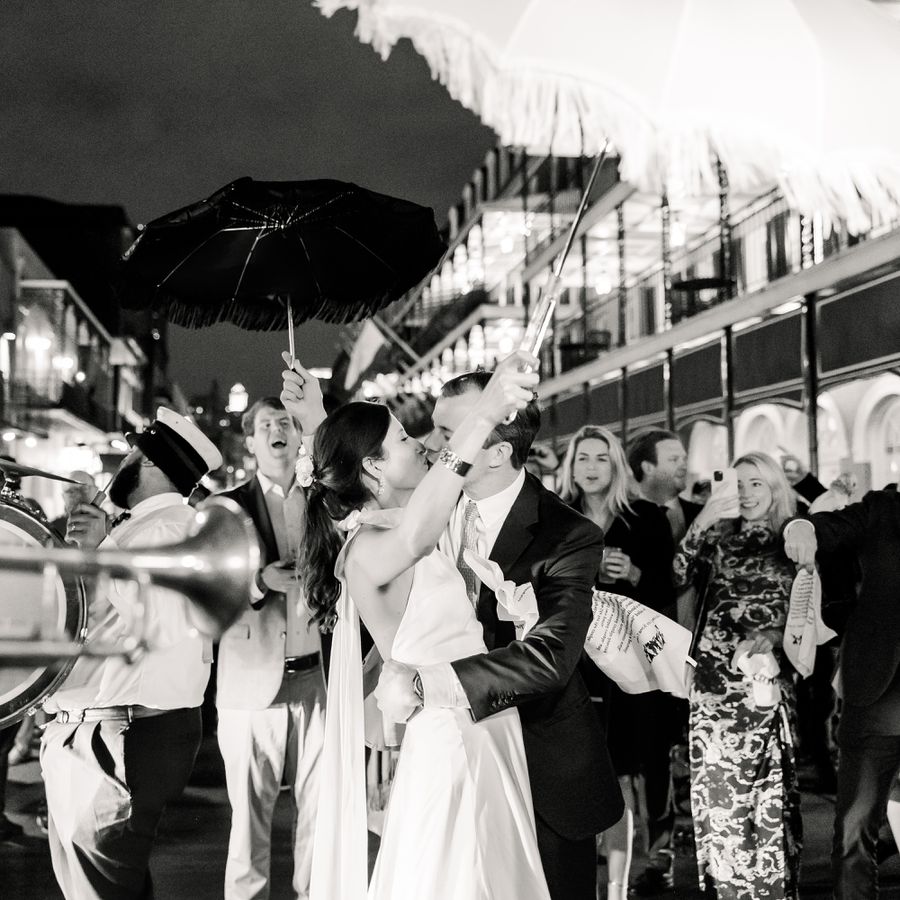 Bride and Groom Kissing While Holding Feathered Umbrellas During Second Line Parade