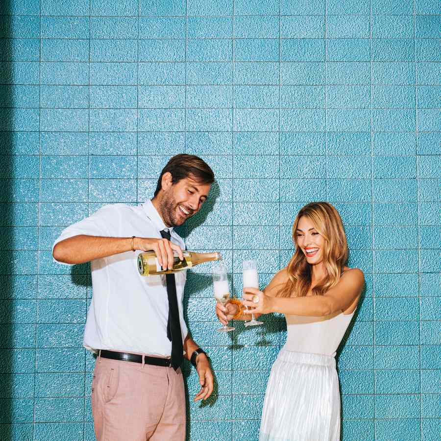 Person pouring champagne into glasses held by another person in front of blue tile wall