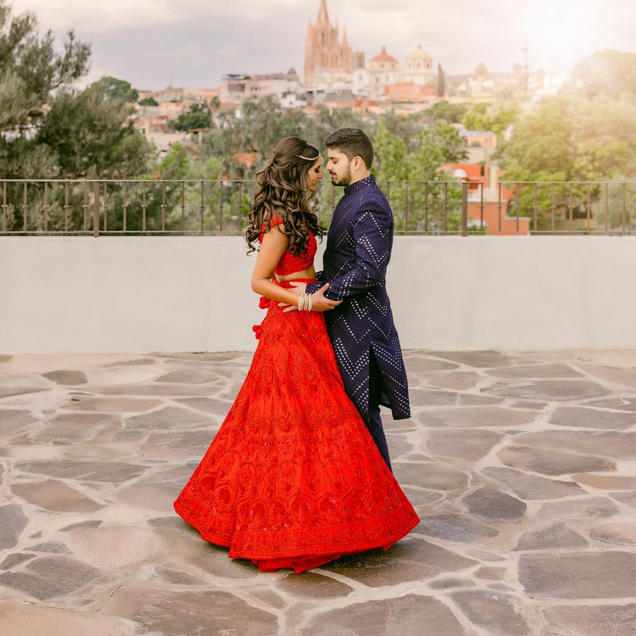 bride wearing a red lengha and groom wear navy blue attire staring into each other's eyes for their wedding portrait